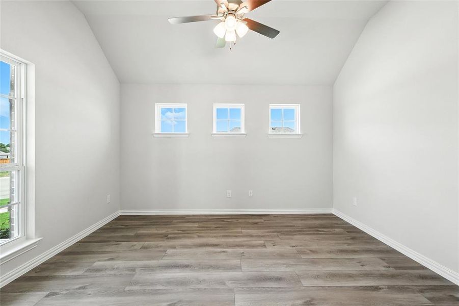 Empty room with vaulted ceiling, plenty of natural light, a ceiling fan, and wood finished floors