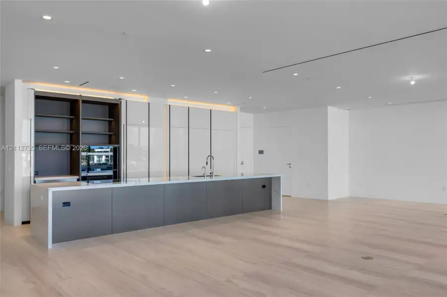 Modern kitchen featuring a expansive island with stone waterfall countertops, high-gloss white cabinetry, integrated open shelving, matte-finish lower cabinetry, and wood-finish flooring