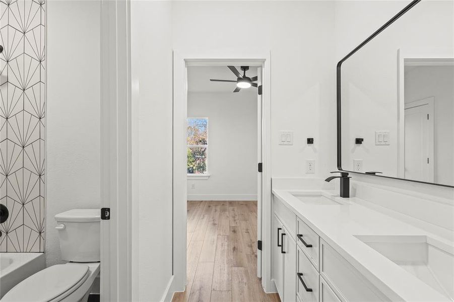 Bathroom with double vanity, shower / bath combination, light wood finished floors, and a ceiling fan