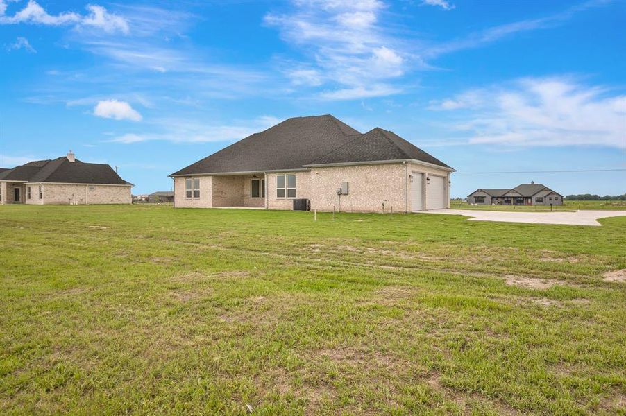 Back of house featuring concrete driveway, an attached garage, central air condition unit, and a yard Back of house featuring concrete driveway, an attached garage, central air condition unit, and a yard