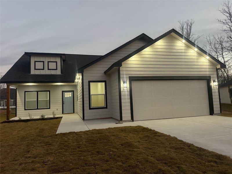 View of front facade featuring an attached garage, driveway, a front lawn, and roof with shingles