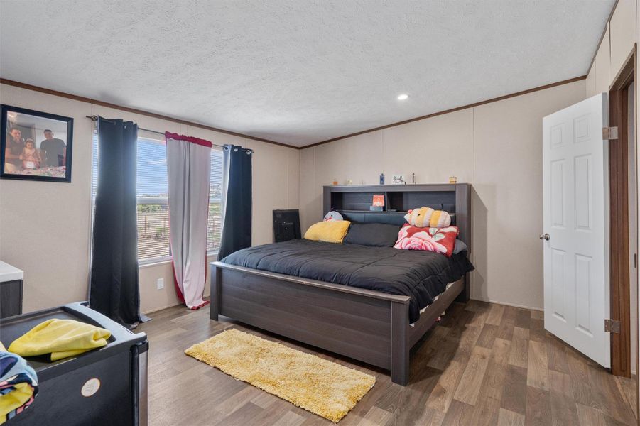 Crown molding frames the bedroom highlighting the wood-look flooring and dual window openings.