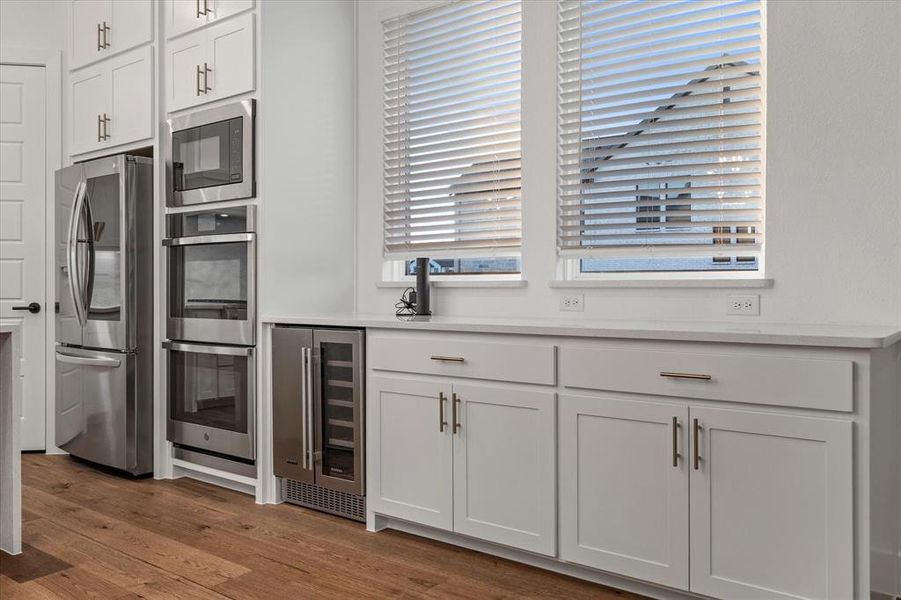 Kitchen featuring white cabinetry, appliances with stainless steel finishes, beverage cooler, and dark wood-style flooring Kitchen featuring white cabinetry, appliances with stainless steel finishes, beverage cooler, and dark wood-style flooring