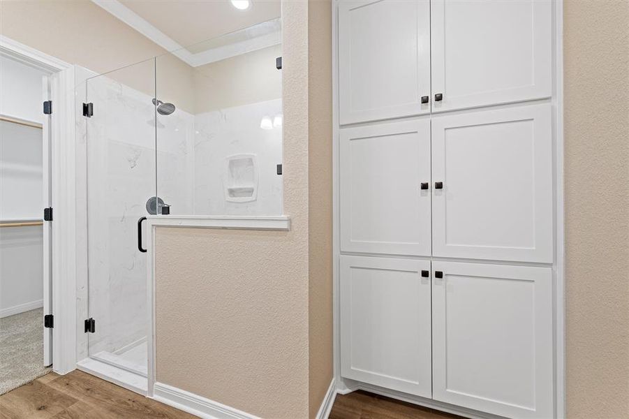 Full bath featuring a marble finish shower, ornamental molding, wood finished floors, a walk in closet, and a textured wall