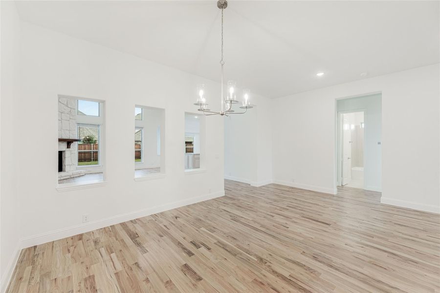 Empty dining room with light wood floors, chandelier, and pass-through windows to adjacent room