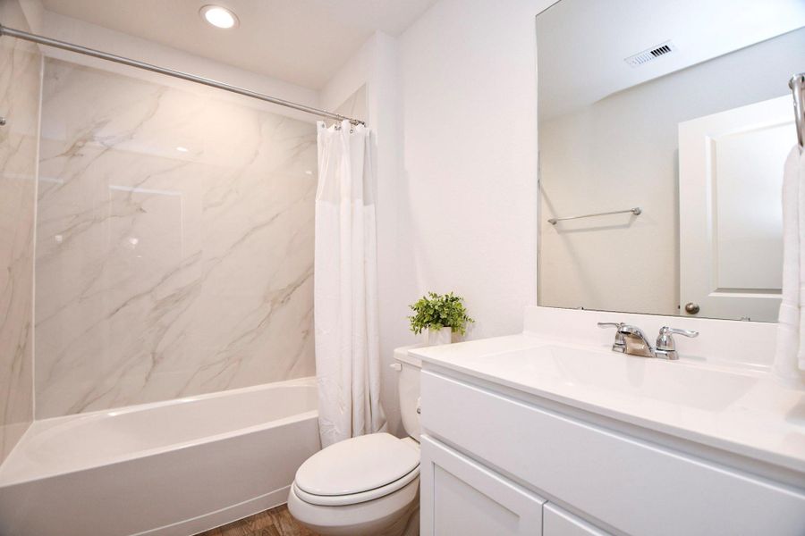 This bathroom includes   elegant, marble-like tile. It has a bright, clean look, complemented by chrome fixtures and bright LED lighting