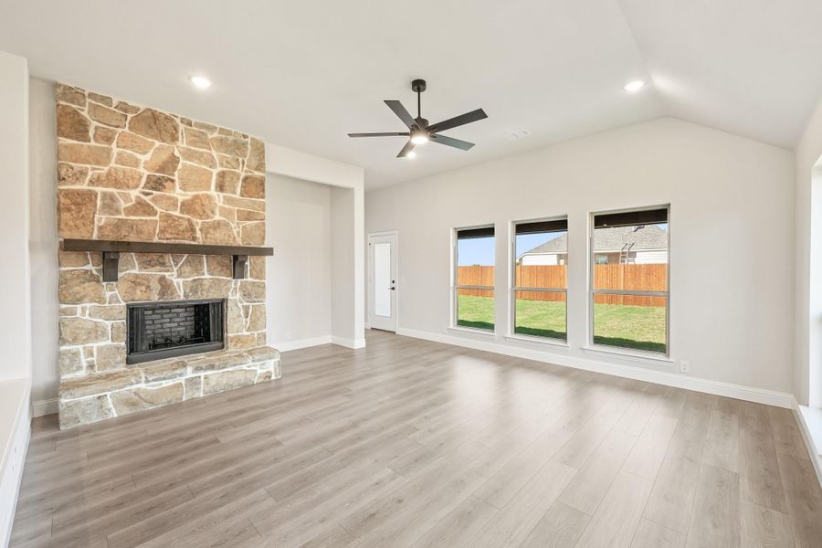 Open living room with floor-to-ceiling stone fireplace, vaulted ceiling, ceiling fan, and hardwood floors Open living room with floor-to-ceiling stone fireplace, vaulted ceiling, ceiling fan, and hardwood floors