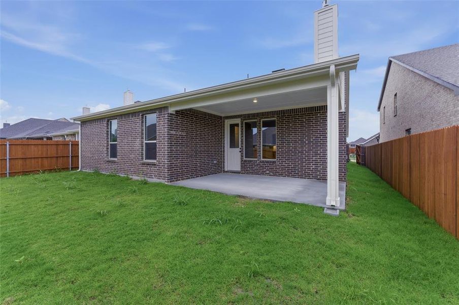 Expansive green lawn featuring a covered patio with concrete flooring, a brick exterior, multiple windows, and a wood privacy fence