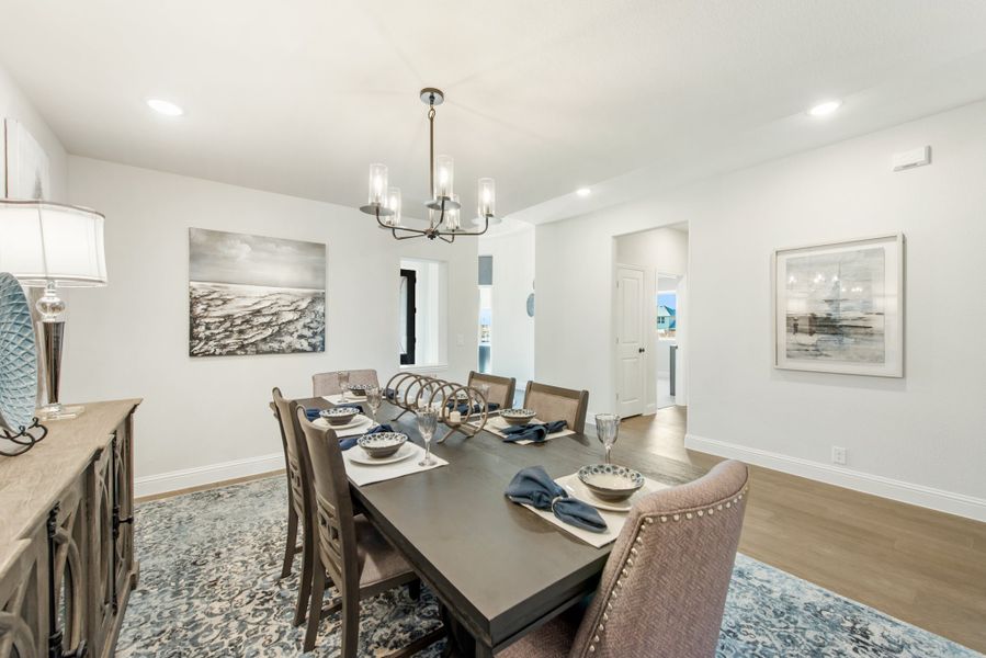 Formal dining room with dark wood table, upholstered chairs, chandelier, and hardwood floors on a patterned area rug
