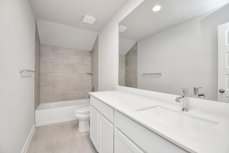 Secondary bath features tile flooring, bath/shower combo with tile surround, light stained wood cabinets, beautiful light countertop. Sample photo of completed home with similar floor plan. Actual colors and selections may vary.