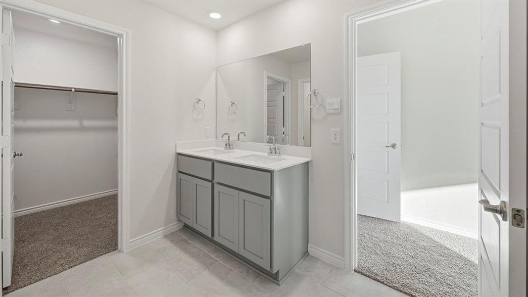 Well-appointed bathroom featuring a double vanity with gray cabinetry and a large mirror, with direct access to a closet space and a room with carpeting