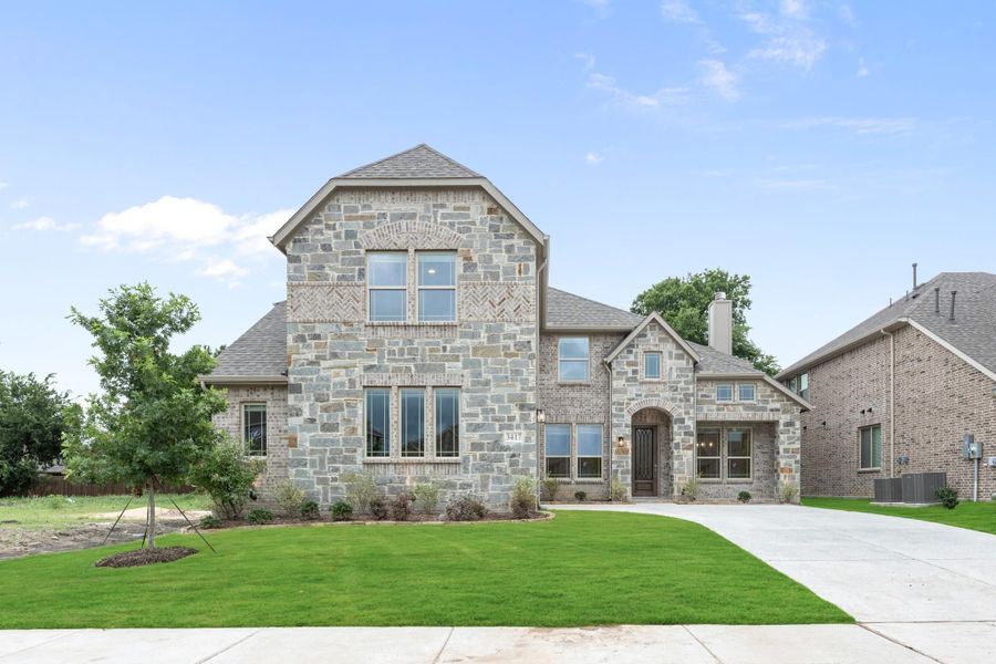 Two-story home with stone and brick exterior, arched entry, and concrete driveway with green lawn Two-story home with stone and brick exterior, arched entry, and concrete driveway with green lawn