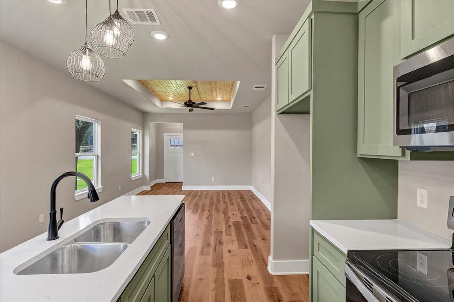 Kitchen with green cabinets, a tray ceiling, appliances with stainless steel finishes, light wood finished floors, and recessed lighting Kitchen with green cabinets, a tray ceiling, appliances with stainless steel finishes, light wood finished floors, and recessed lighting