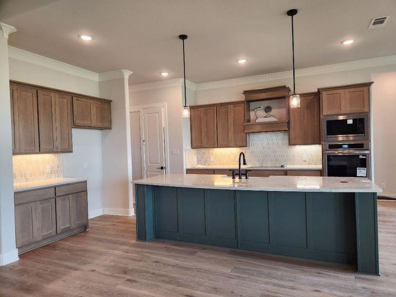 Spacious kitchen featuring a large central island, wood-finish flooring, recessed lighting, and pendant fixtures