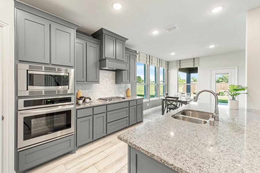 Kitchen with gray cabinets, granite countertops, stainless steel appliances, and island sink with backyard view