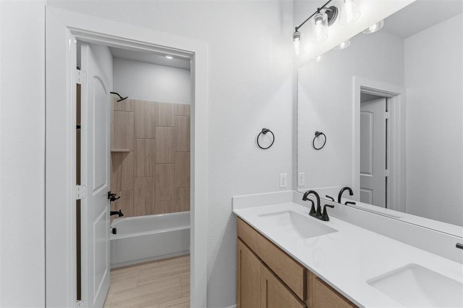 Full bath featuring double vanity, shower / bathtub combination, and light wood-type flooring