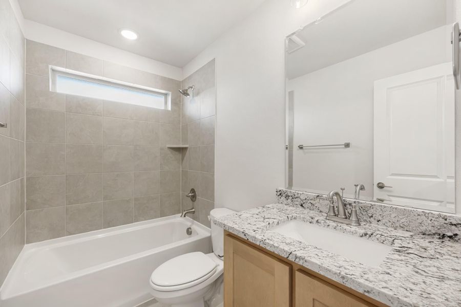 Bathroom with granite countertop vanity, tiled tub-shower combo, and toilet