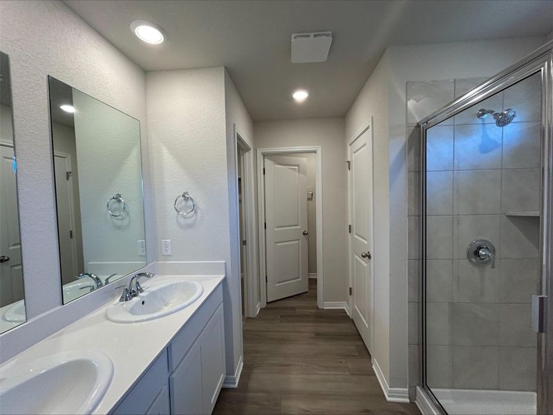 Bathroom featuring double vanity, wood finished floors, a shower stall, and recessed lighting