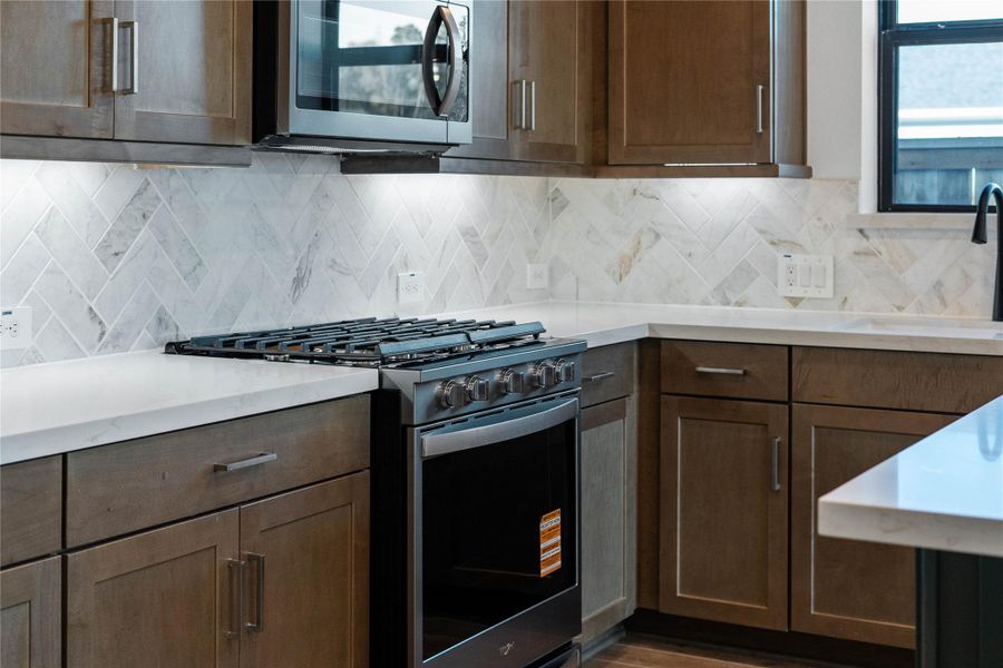 Professional-grade gas range with a substantial cooktop and integrated griddle, perfectly complemented by a coordinating over-the-range microwave. These high-end finishes, set against crisp white quartz countertops and a elegant herringbone backsplash, combine to create an inviting and highly functional space perfect for entertaining. Professional-grade gas range with a substantial cooktop and integrated griddle, perfectly complemented by a coordinating over-the-range microwave. These high-end finishes, set against crisp white quartz countertops and a elegant herringbone backsplash, combine to create an inviting and highly functional space perfect for entertaining.