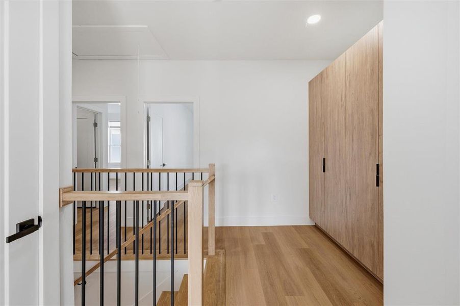 Staircase Landing features recessed lighting throughout the space. Built-in storage cabinets provide additional organization. Wood and black metal railing overlooks the staircase below. Vinyl flooring extends throughout.