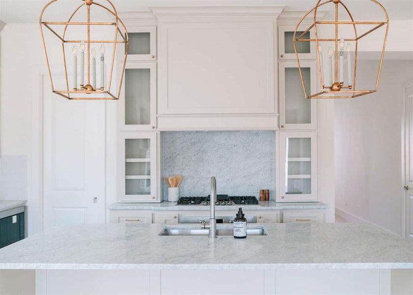 Kitchen featuring decorative backsplash, light stone countertops, sink, a center island with sink, and white cabinetry