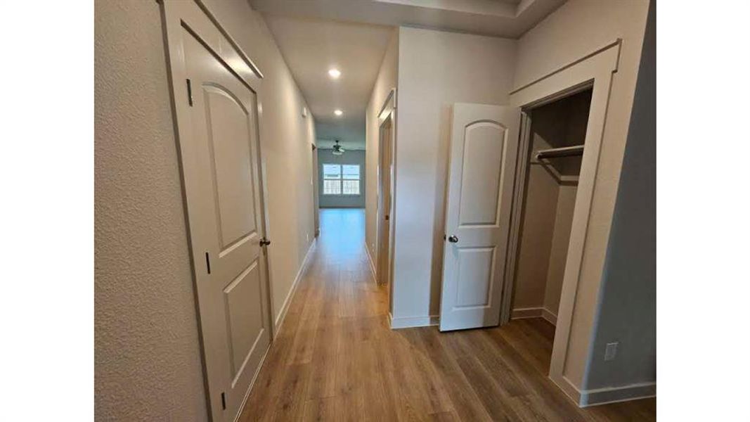 Hallway featuring wood-finish flooring, recessed lighting, and a tray ceiling detail Hallway featuring wood-finish flooring, recessed lighting, and a tray ceiling detail