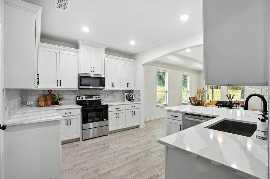 Kitchen with tasteful backsplash, stainless steel appliances, recessed lighting, light wood-style flooring, and white cabinetry