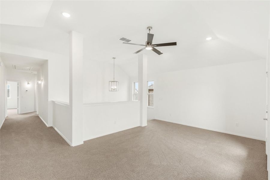 Open living area with ceiling fan, pendant light, beige carpet, and hallway leading to entry Open living area with ceiling fan, pendant light, beige carpet, and hallway leading to entry