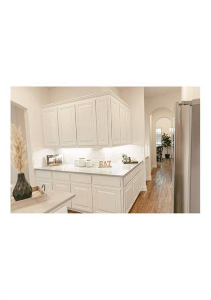 Kitchen with white cabinetry, backsplash, light hardwood / wood-style flooring, and stainless steel refrigerator