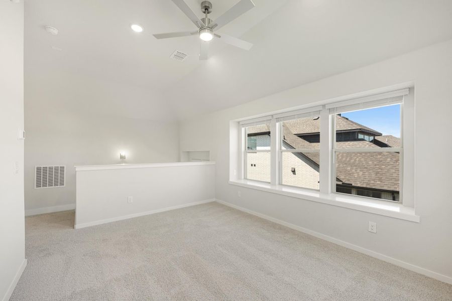 Empty bedroom with vaulted ceiling, ceiling fan, carpet flooring, and large triple window