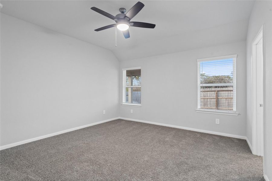 The primary bedroom provides a peaceful escape with a bright, neutral palette, sloped ceilings, large windows, and plush carpet flooring, creating a calm and restorative atmosphere to end your day.