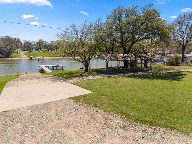 View of grassy yard with a boat ramp, a patio area, a dock, and a water view