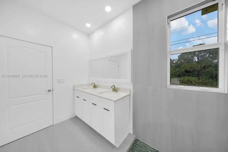 Dual-sink vanity with light-toned countertop, gold-tone fixtures, recessed lighting, and large-format tile wall treatments