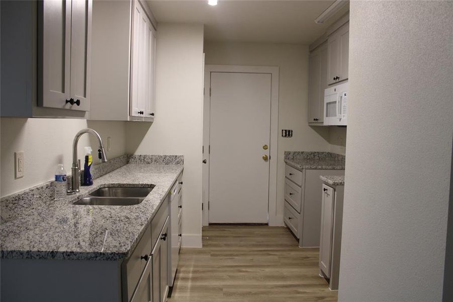 Kitchen with light stone counters, light wood-style flooring, white appliances, and gray cabinets