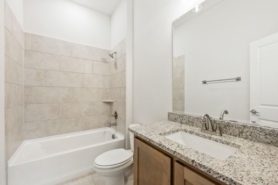 Bathroom with tiled tub-shower combo, granite vanity countertop, and wood cabinets Bathroom with tiled tub-shower combo, granite vanity countertop, and wood cabinets