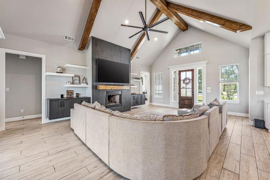 Living area with high vaulted ceiling, ceiling fan, a large fireplace, light wood-style floors, and beam ceiling