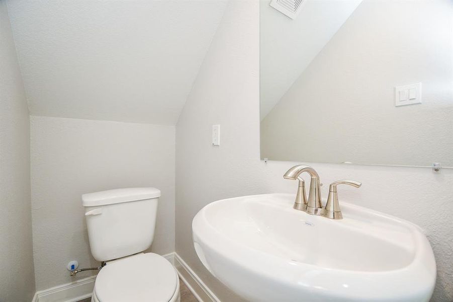 This is a compact half-bathroom featuring a pedestal sink with a modern faucet and a toilet, set against neutral walls with an angled ceiling, suggesting it's located under a staircase.