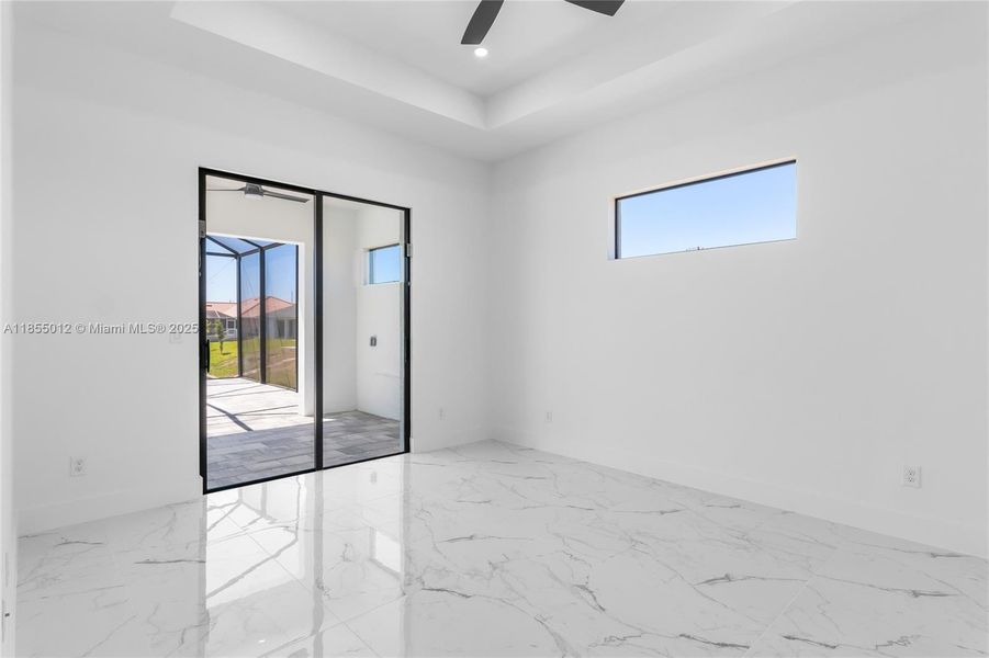 Bright and Airy Primary w a view turing baseboards, marble finish floor, ceiling fan, and a raised ceiling