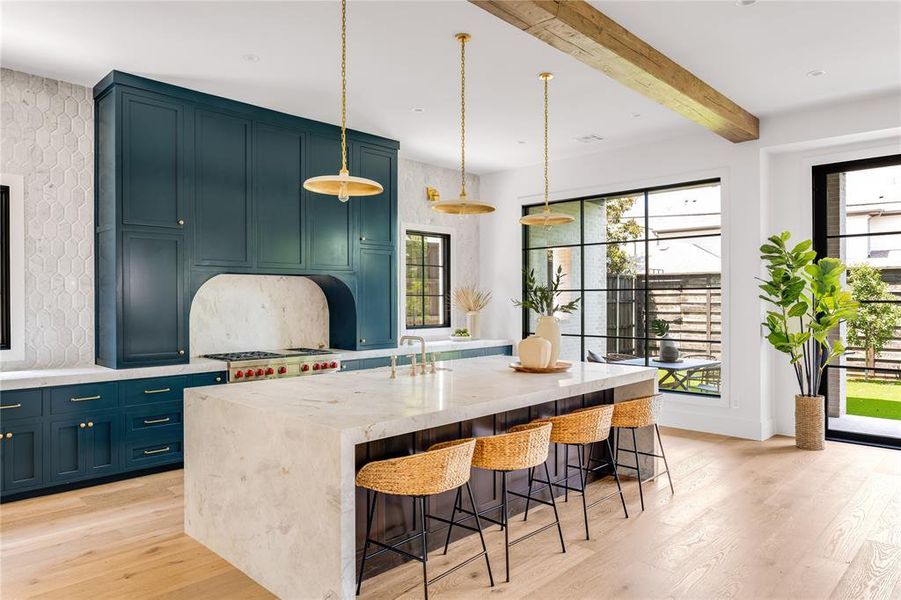 Kitchen with a breakfast bar area, light hardwood / wood-style floors, a kitchen island with sink, and light stone countertops