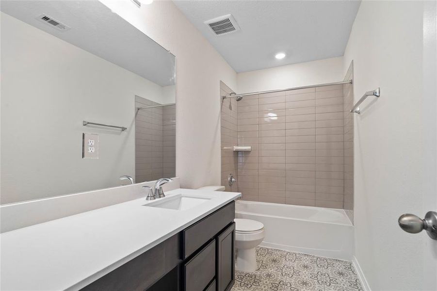 Secondary bath features tile flooring, bath/shower combo with tile surround, stained wood cabinets, beautiful light countertops, mirror, sleek fixtures and modern finishes.