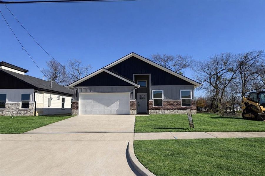 View of front of home with a front yard, an attached garage, concrete driveway, board and batten siding, and brick siding View of front of home with a front yard, an attached garage, concrete driveway, board and batten siding, and brick siding