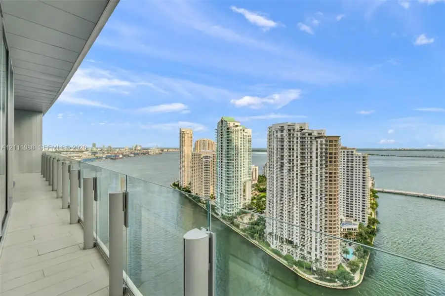 Covered balcony with light-toned flooring, frameless glass balustrades, and expansive water and urban skyline scenery Covered balcony with light-toned flooring, frameless glass balustrades, and expansive water and urban skyline scenery
