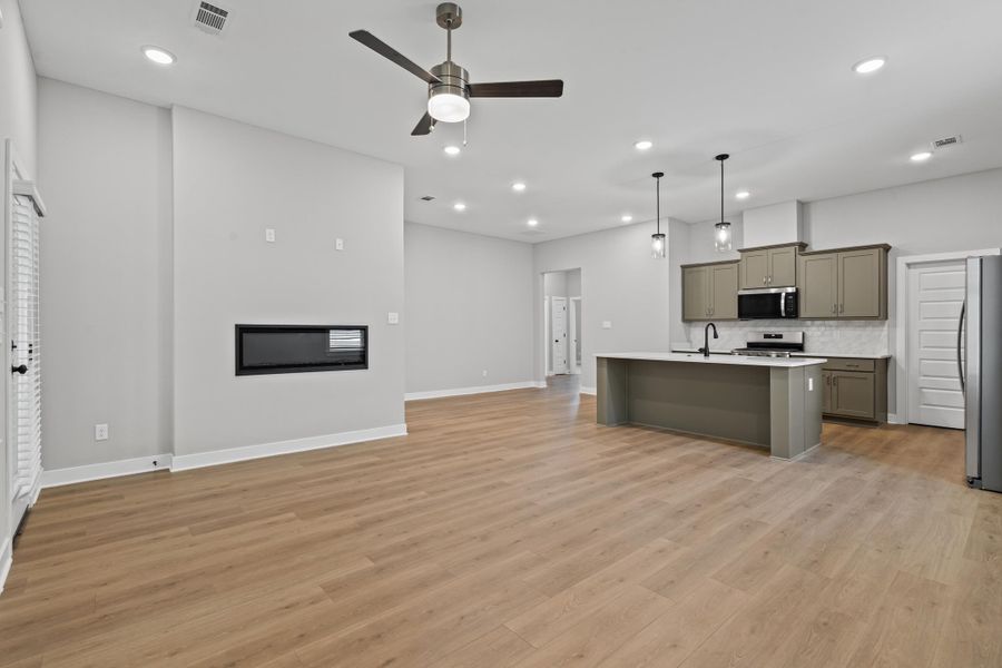 Kitchen with decorative light fixtures, open floor plan, tasteful backsplash, stainless steel appliances, and light wood-type flooring
