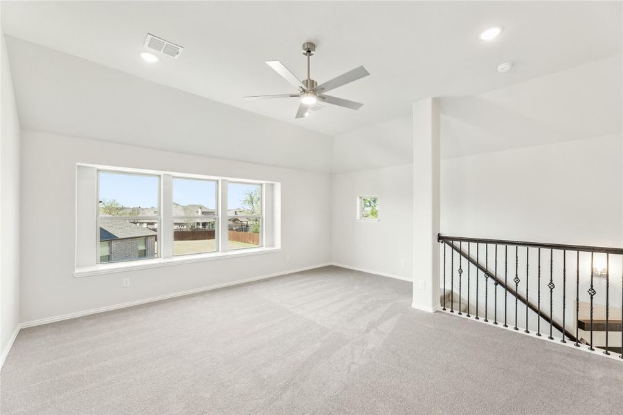 Open upstairs loft with carpet, ceiling fan, large windows, and iron stair railing
