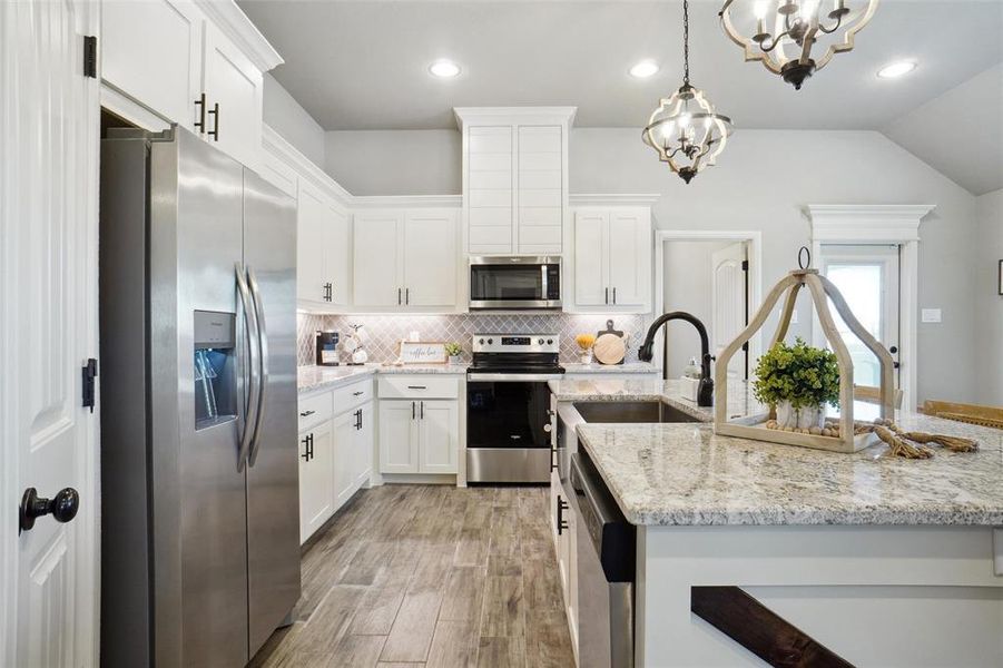 Kitchen with decorative backsplash, appliances with stainless steel finishes, light hardwood / wood-style floors, decorative light fixtures, and sink