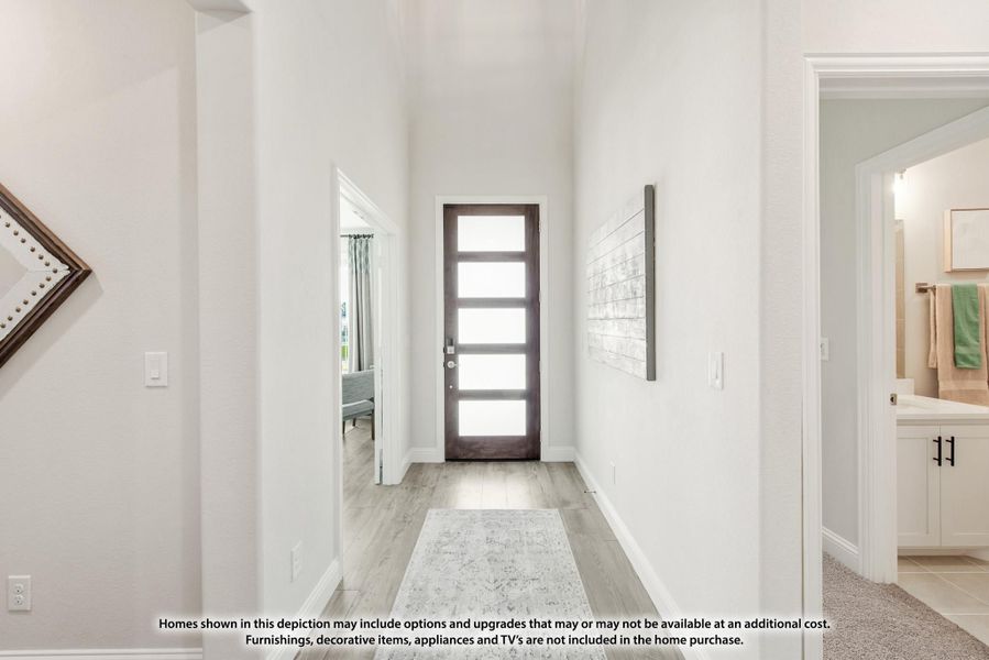Bright entryway hallway with dark wood glass-panel front door, light wood floors, and high white walls