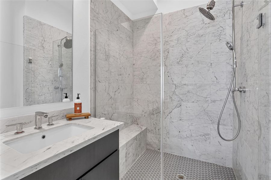 Marble-clad shower features a rainfall head, handheld sprayer, and built-in bench.