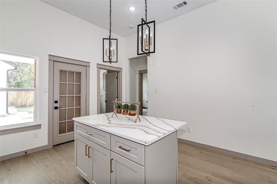 Kitchen with light wood-style flooring, light stone counters, pendant lighting, a center island, and a chandelier