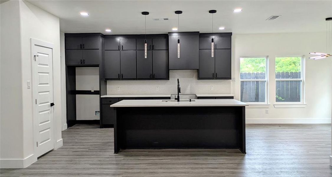 Kitchen with a sink, baseboards, light countertops, and an island with sink