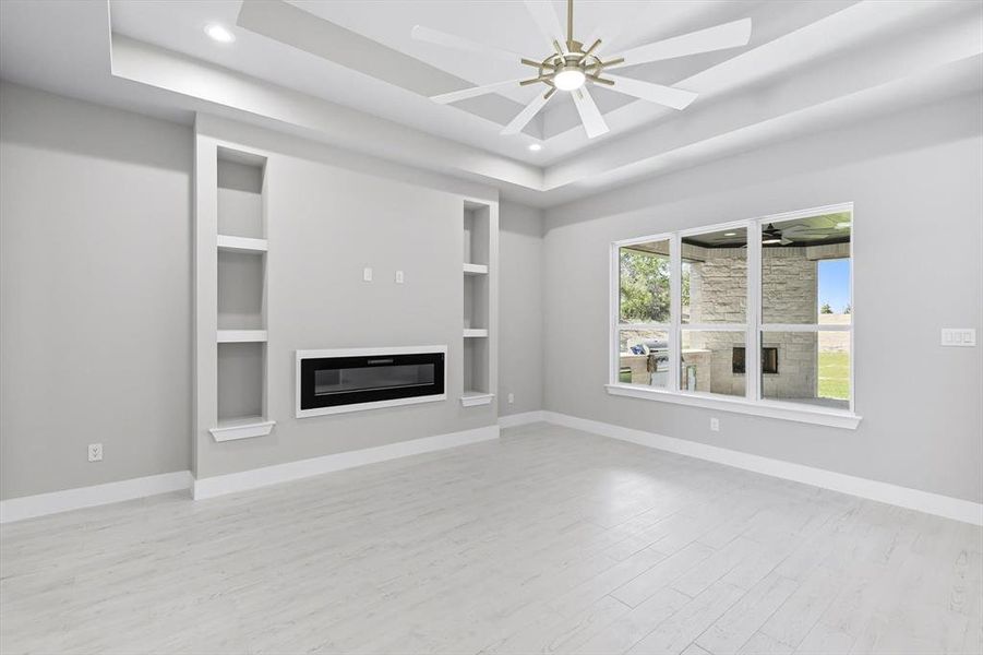 Unfurnished living room featuring a glass covered fireplace, light wood-type flooring, ceiling fan, a tray ceiling, and recessed lighting